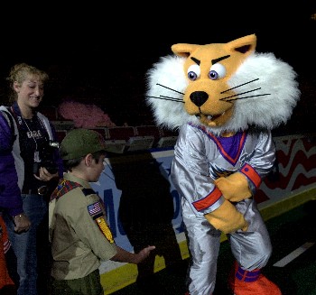 A club mascot in a silver and orange suit greets two supporters at the boards during an arena night, photographed for MISL.net.